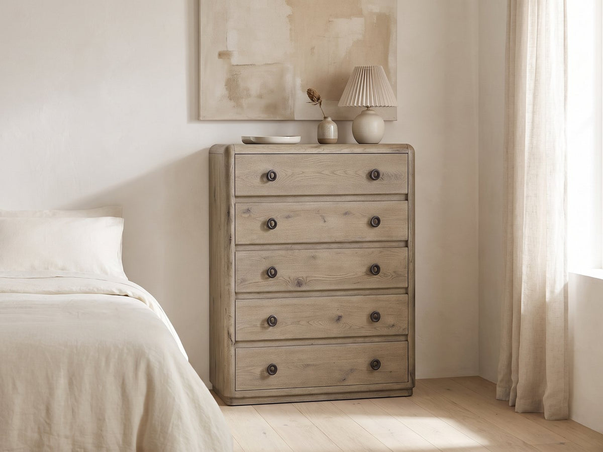 Maniago 42-Inch Weathered Natural Oak 5-Drawer Chest against a plaster wall under an abstract canvas in a bright bedroom