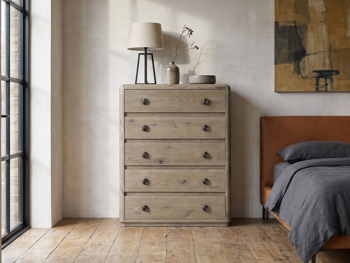 Maniago 42-Inch Weathered Natural Oak 5-Drawer Chest against a plaster wall in an industrial loft bedroom