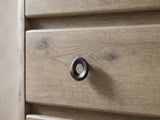 Close-up of the Maniago 42-Inch Weathered Natural Oak 5-Drawer Chest: a dark cast-iron oval ring pull on a knotty oak drawer front beside the rounded case edge