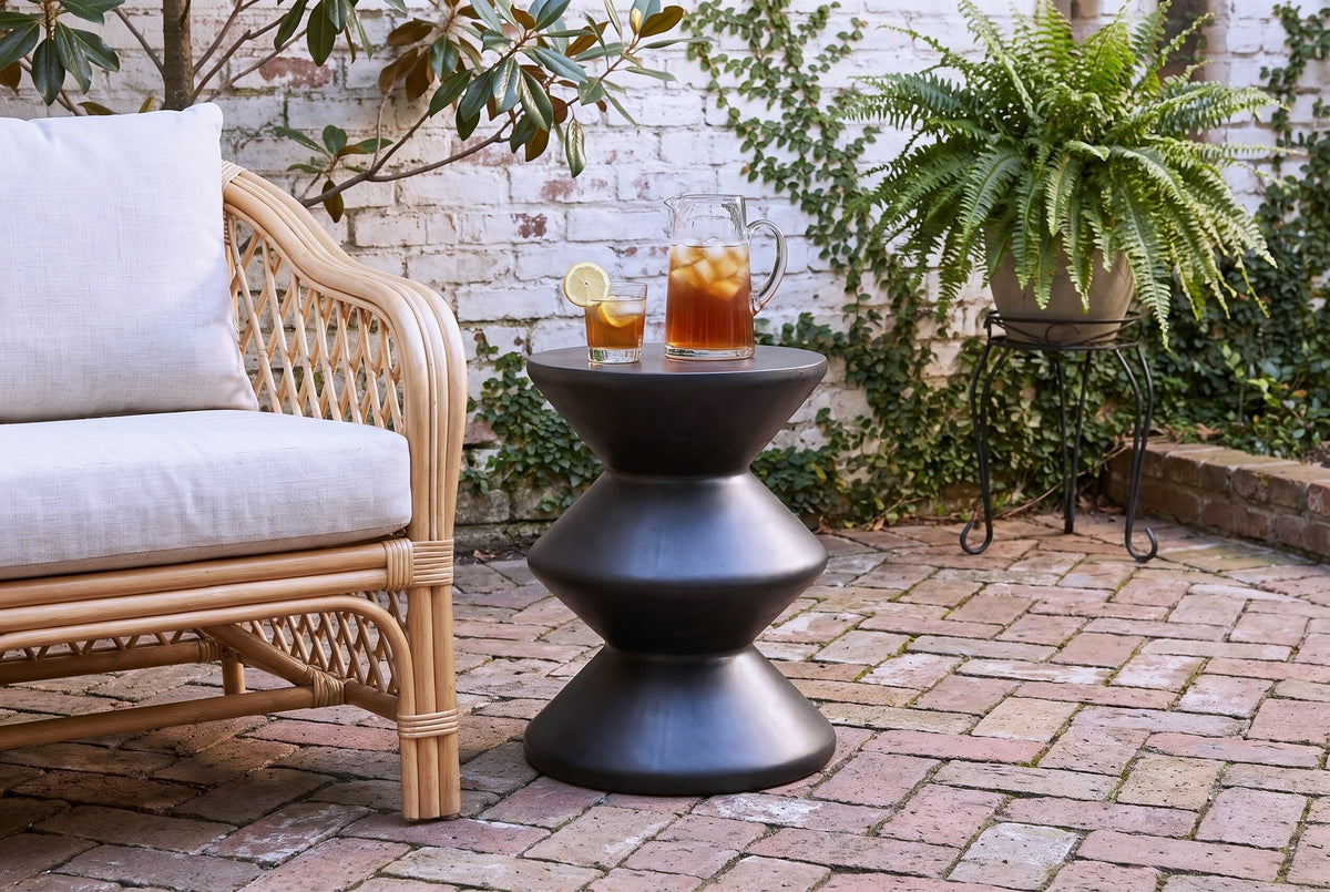 Marineo black concrete zigzag side table with a pitcher of iced tea and a glass beside a rattan armchair in a Savannah, Georgia courtyard, a whitewashed brick wall with creeping fig and herringbone brick paving (chair and decor not included)