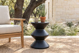 Marineo black concrete zigzag side table with a stoneware mug and a pot of rosemary beside a teak lounge chair on a decomposed granite patio in the Texas Hill Country, a cream limestone wall, feather grass and live oaks behind (chair and decor not included)