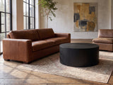 Marostica Black Mango Drum Coffee Table seen from the side, on a vintage rug in front of a leather sofa in an industrial loft