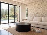 Marostica Black Mango Drum Coffee Table on a jute rug in front of a linen sofa in a poolside villa