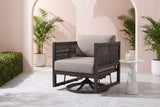 The Marsala swivel glider lounge chair in dark brown with taupe cushions in a Coral Gables courtyard with a blush-pink stucco wall, arched openings, white marble pavers and potted palms (side table not included)