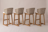 The four Mascali stools from behind: the curved open-lattice wicker backs, the acacia legs and the rounded back corners of the sled runners