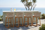 Four Mascali acacia bar stools at a sage-green board-and-batten bar with a white quartz top on a slate terrace in Laguna Beach, the Pacific beyond a glass rail (bar counter not included)
