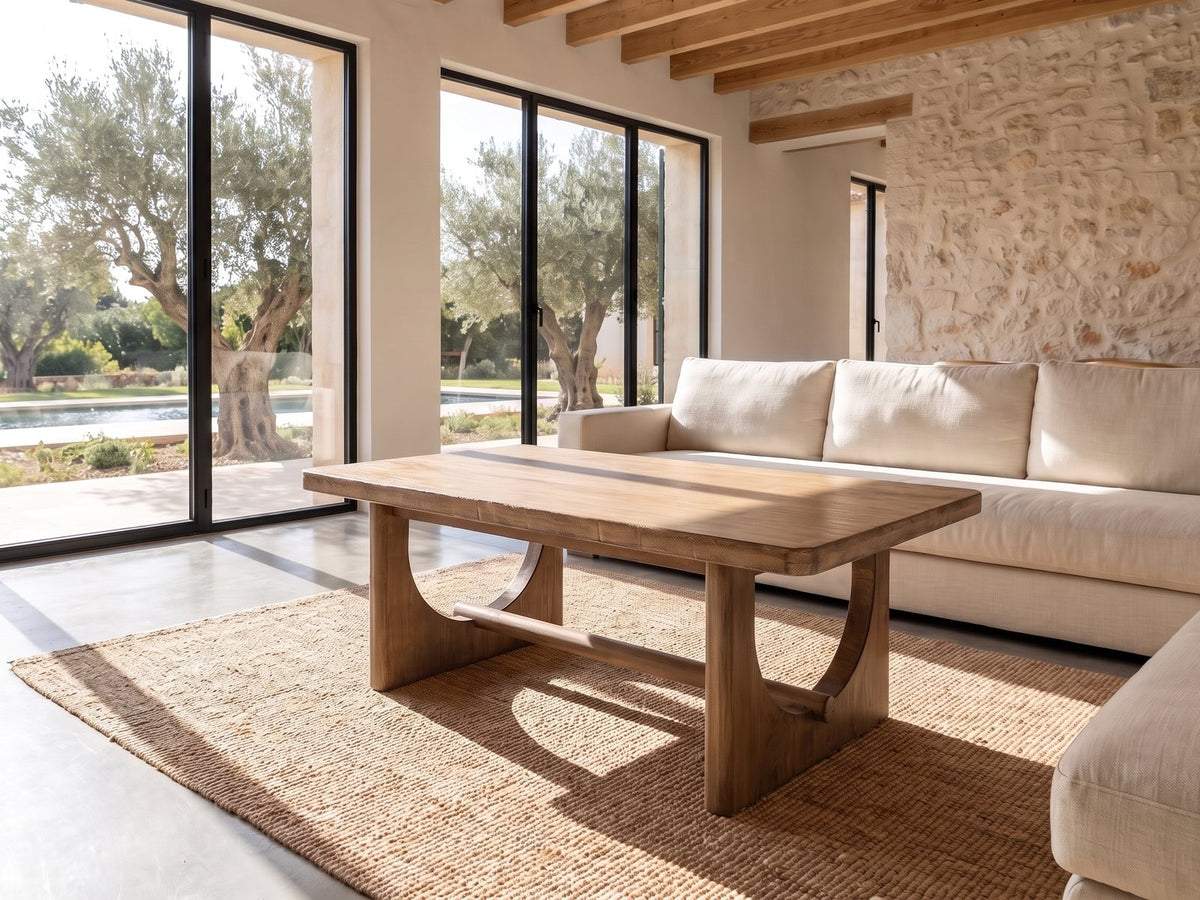 Matelica Reclaimed Pine Trestle Coffee Table seen from the side, on a jute rug in front of a linen sofa in a poolside villa