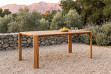 Mazara acacia outdoor dining table on pale gravel in an Ojai garden at golden hour, a dry-stacked river-stone wall, olive trees, lavender and the mountains behind (chairs not included)