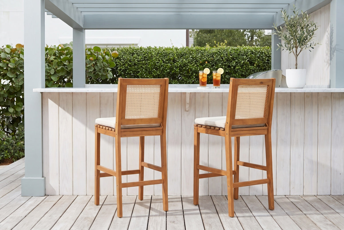 Two Mazzarino acacia bar stools at a whitewashed cypress bar with a white marble top under a grey-blue pergola in a Rosemary Beach courtyard, a sea grape hedge behind (bar counter not included)