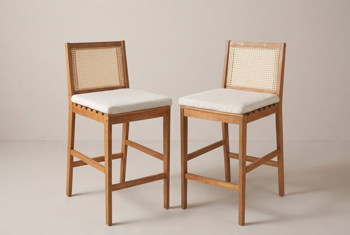 The two Mazzarino acacia bar stools with cane backs and pale beige cushions, three-quarter view on a light studio backdrop
