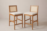 The two Mazzarino acacia bar stools with cane backs and pale beige cushions, three-quarter view on a light studio backdrop