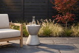 Mazzaro concrete hourglass side table on dark slate pavers in a Houston garden, a black slatted fence, ornamental grasses and a red Japanese maple behind (chair not included)