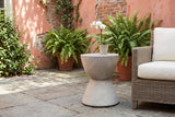 Mazzaro concrete side table in a New Orleans courtyard with a coral plaster wall, ferns and bluestone flagstones, beside a woven armchair (chair and orchid not included)