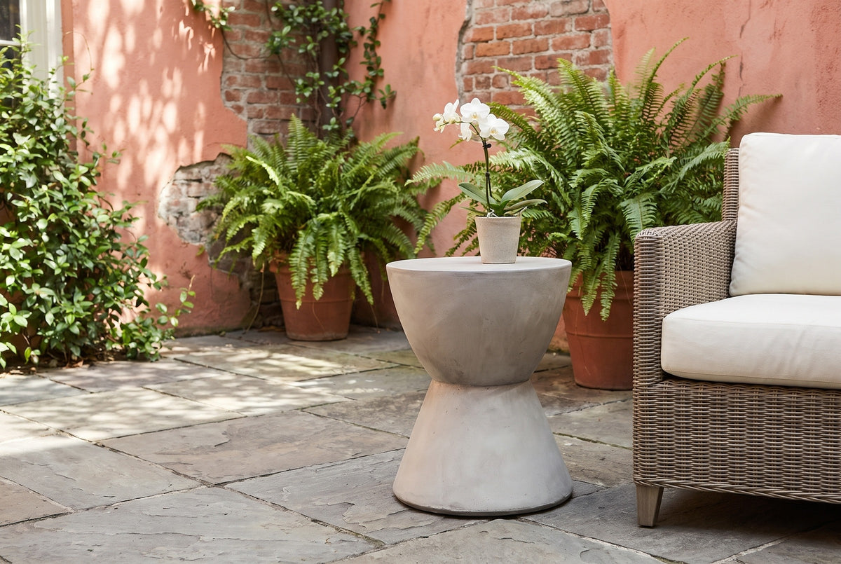 Mazzaro concrete side table in a New Orleans courtyard with a coral plaster wall, ferns and bluestone flagstones, beside a woven armchair (chair and orchid not included)