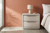 Melfi gray oak two-drawer nightstand with a ceramic lamp beside a bed in a Palm Springs bedroom with a terracotta clay plaster wall, a polished concrete floor and a palm shadow