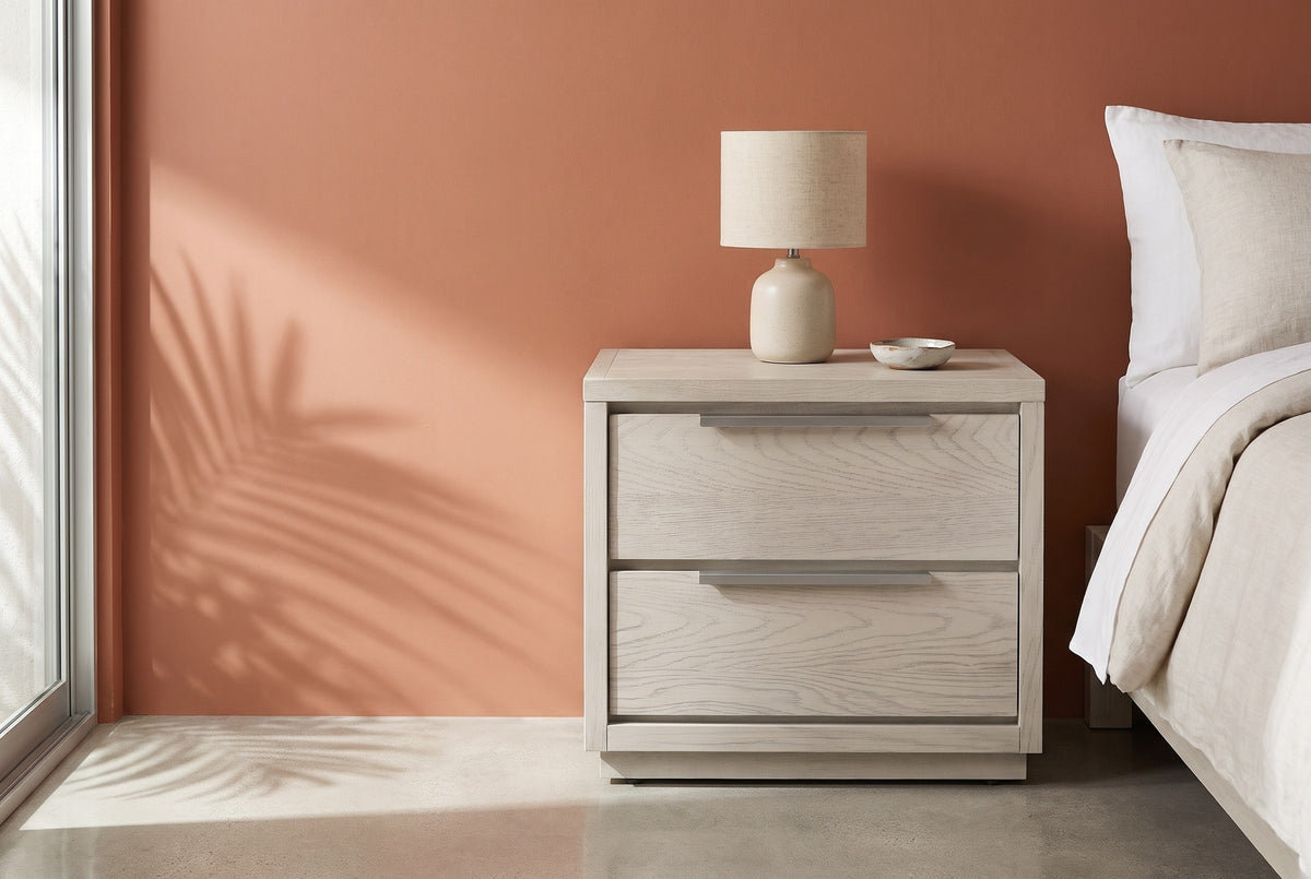 Melfi gray oak two-drawer nightstand with a ceramic lamp beside a bed in a Palm Springs bedroom with a terracotta clay plaster wall, a polished concrete floor and a palm shadow