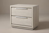 The Melfi two-drawer nightstand in wire-brushed gray oak with long brushed metal edge pulls and a low plinth, three-quarter view on a warm studio backdrop