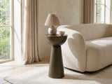 Melpignano Antique Gold Iron Pedestal Side Table with a lamp and a ceramic bowl beside a cream boucle sofa in a bright plaster room