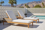 The Menfi set of two acacia chaise loungers on a terrazzo pool deck in Palm Springs, a white breeze-block wall and the mountains behind (side table and towel not included)
