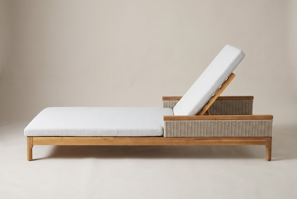 One Menfi chaise lounger seen from the side: the long low acacia frame on round legs, the wicker armrest and the raised backrest at the head end