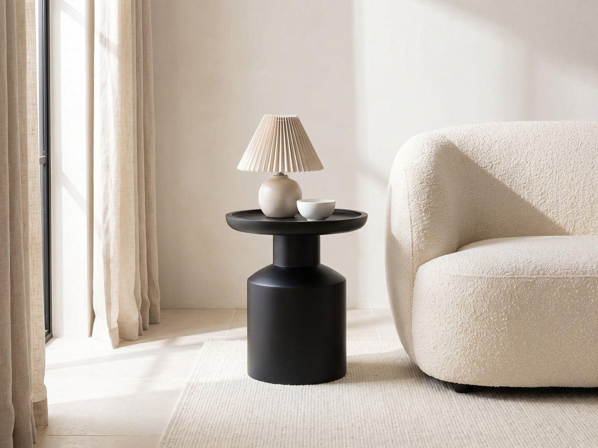 Mesoraca Black Mango Pedestal Side Table with a lamp and a ceramic bowl beside a cream boucle armchair in a bright plaster room