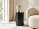 Miglionico Black Mango Wood Faceted Drum Side Table with a lamp and a ceramic bowl beside a cream boucle armchair in a bright plaster room