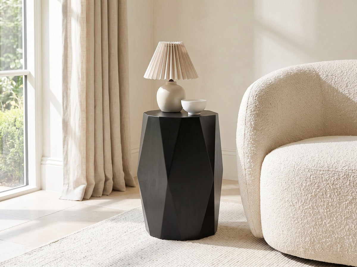 Miglionico Black Mango Wood Faceted Drum Side Table with a lamp and a ceramic bowl beside a cream boucle armchair in a bright plaster room