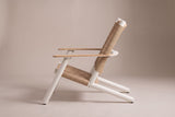 The Militello lounge chair from the side: the front leg leaning back to the flat teak arm, the deep woven seat and the reclined back on long rear runners