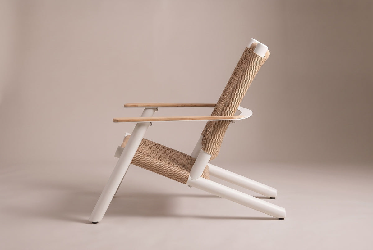 The Militello lounge chair from the side: the front leg leaning back to the flat teak arm, the deep woven seat and the reclined back on long rear runners