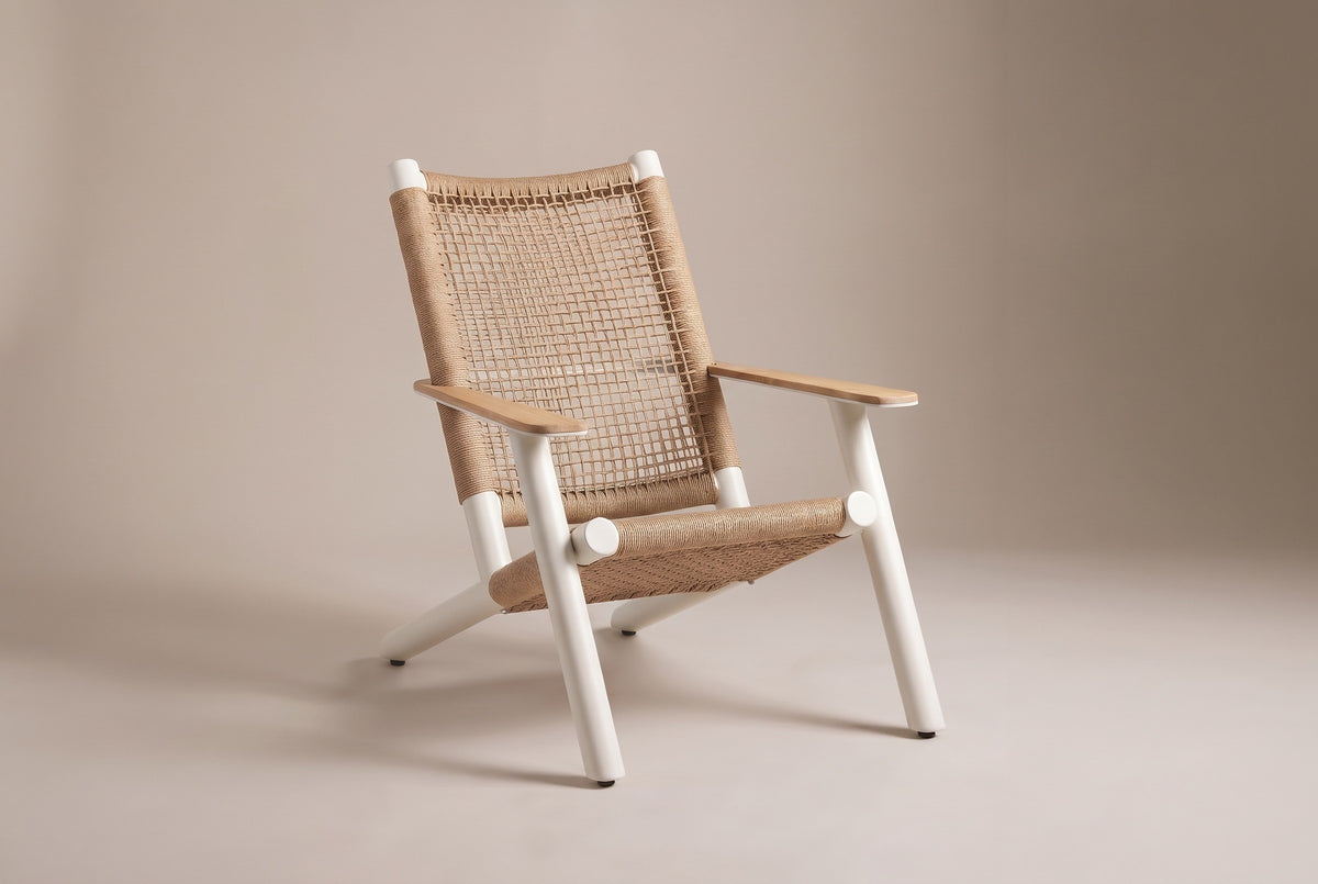 The Militello lounge chair: white aluminum frame, natural beige wicker seat and open-grid back, teak arms, three-quarter view on a light studio backdrop