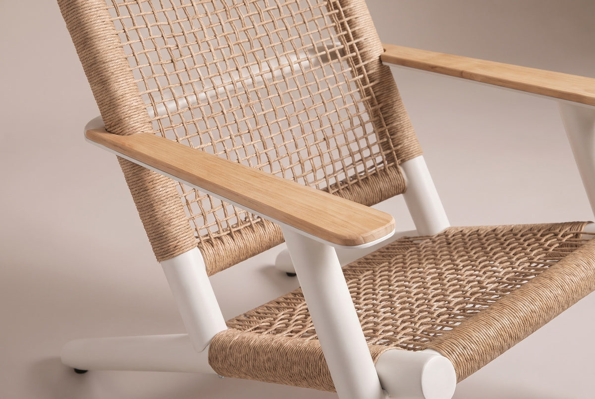 Close-up of the Militello chair: a natural teak arm board on a white aluminum plate, the woven seat and the open-grid wicker back