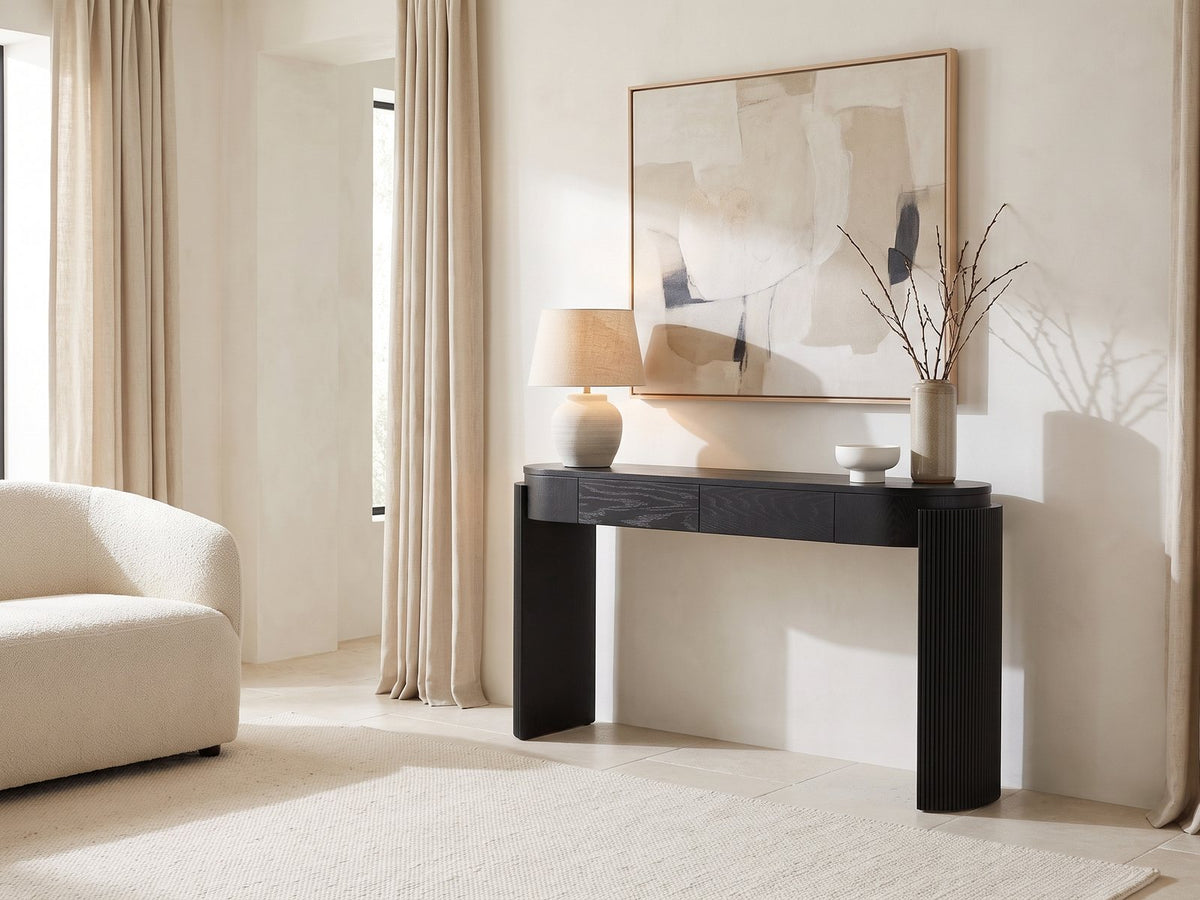 Minervino Black Oak Fluted Racetrack Console Table against a plaster wall under an abstract canvas in a bright living room