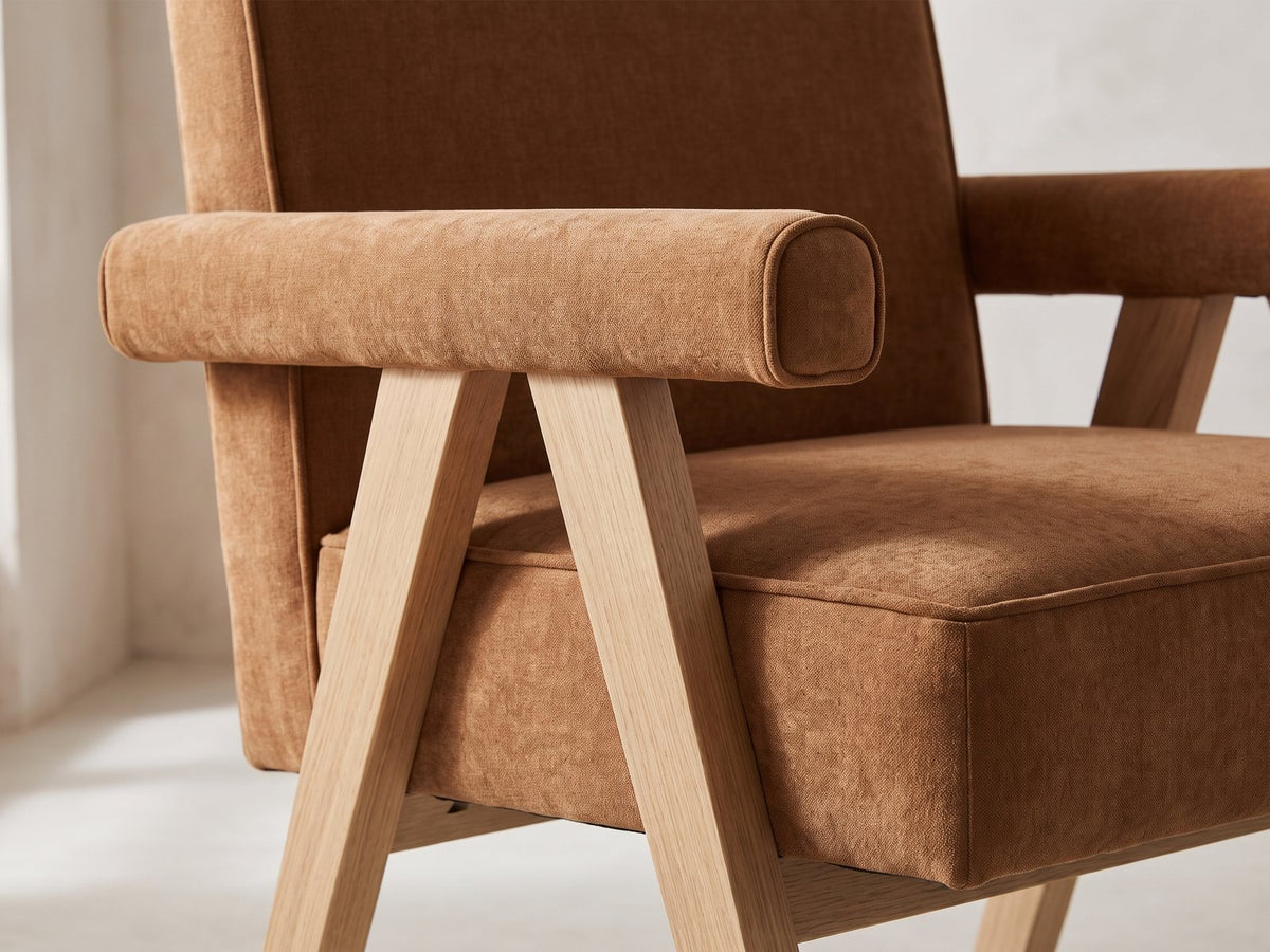 Close-up of the Minturno 95-Inch Light Oak Sled Base Dining Set with 6 Chairs: the padded arm bolster and inverted-V oak leg frame of an armchair in caramel chenille