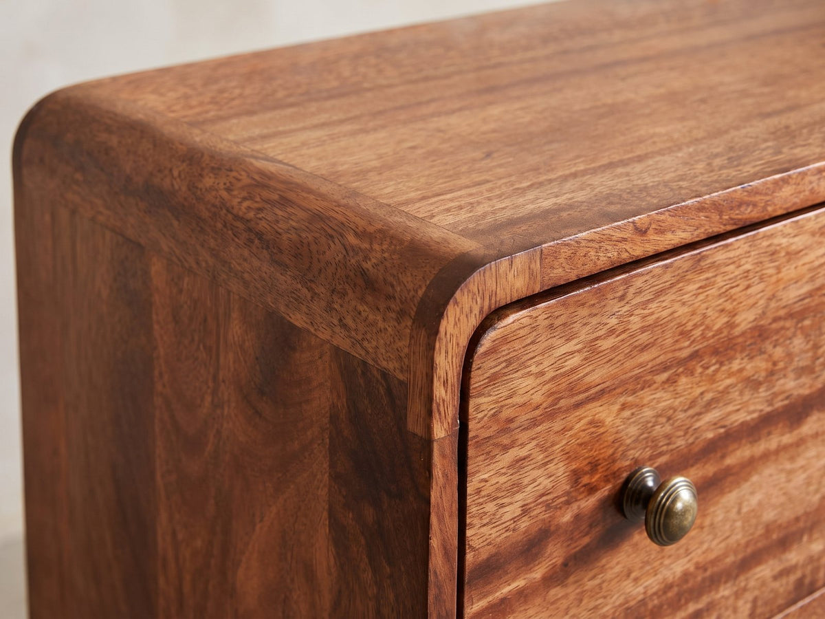 Close-up of the Mira 28-Inch Honey Caramel Solid Mango 3-Drawer Chest: the rounded top corner of the solid mango case and a stepped antique-brass knob