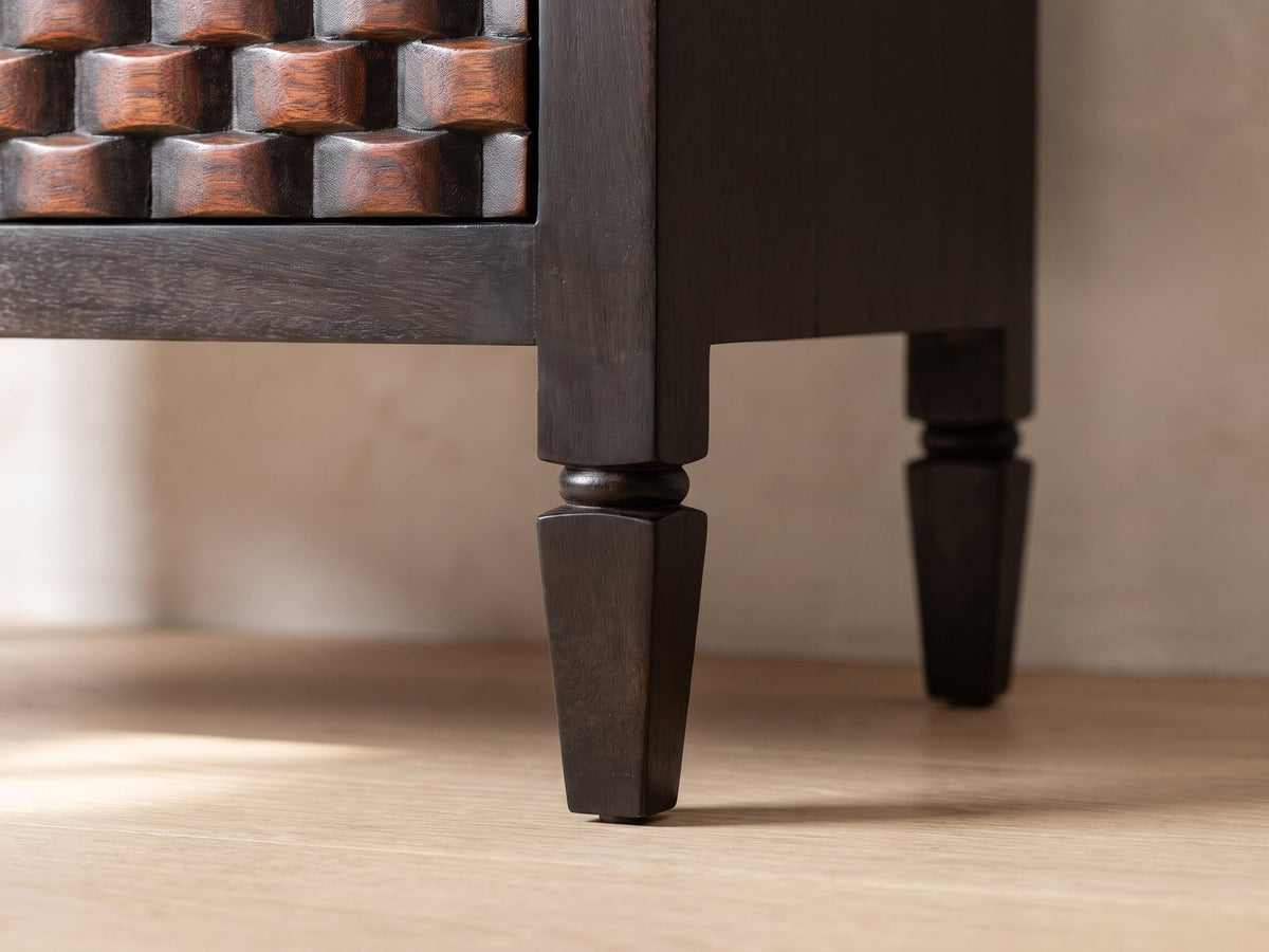 Close-up of the Mirano 33-Inch Velvet Mocha Carved Mango 3-Drawer Chest: a turned and tapered leg under the square corner of the carved chest