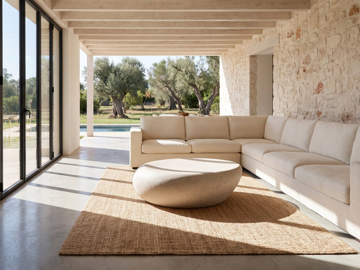Modica Cream Fiberglass Pebble Coffee Table on a jute rug in front of a linen sofa in a poolside villa