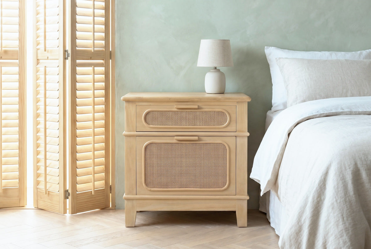 Mogoro pine and cane nightstand against a sage-green plaster wall in a Savannah bedroom with a herringbone floor and wooden shutters