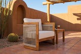 Mondello acacia club chair on a saltillo tile patio in Tucson, Arizona, with a terracotta adobe wall, a log ramada and a barrel cactus behind (side table not included)