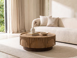 Mondovi 36-Inch Round Carved Limed Ash Drum Coffee Table styled with books, a vase and a stone bowl in front of a cream sofa in a bright plaster room