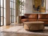 Mondovi 36-Inch Round Carved Limed Ash Drum Coffee Table on a vintage rug in front of a leather sofa in an industrial loft