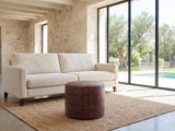 Moneglia Distressed Brown Top-Grain Buffalo Leather Round Pouf on a jute rug in front of a linen sofa in a poolside villa