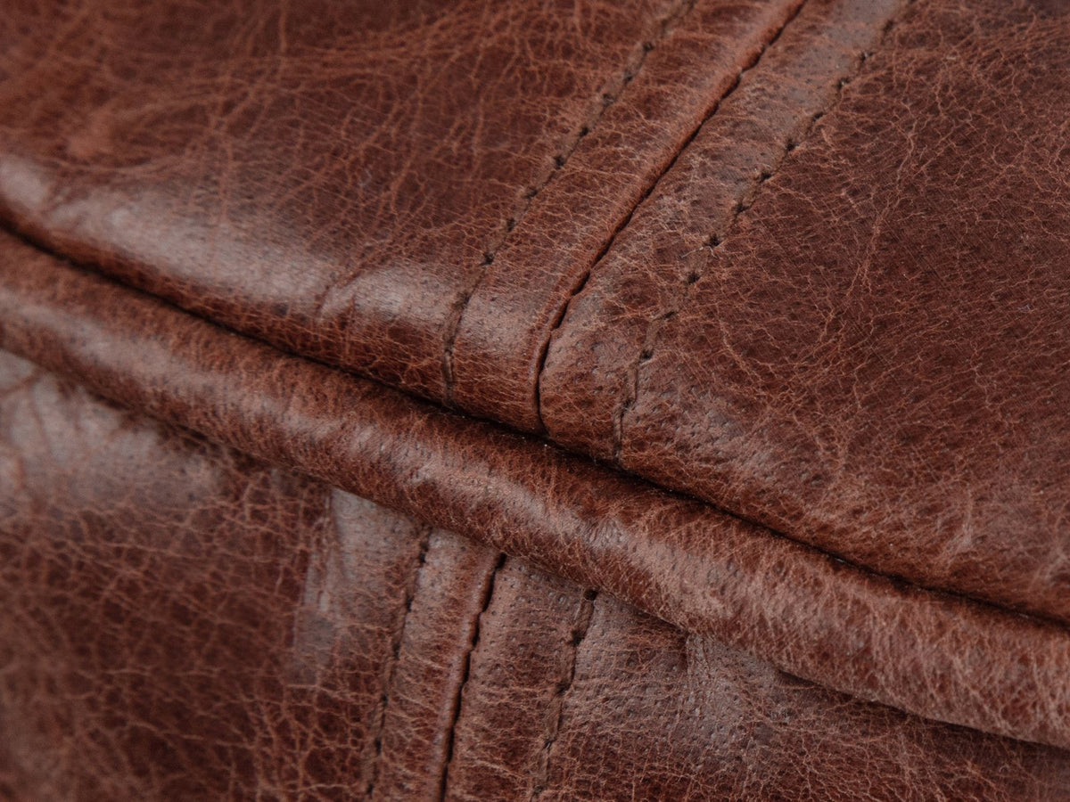 Close-up of the Moneglia Distressed Brown Top-Grain Buffalo Leather Round Pouf: the raw-edged flange lip round the top rim where it meets a topstitched side seam
