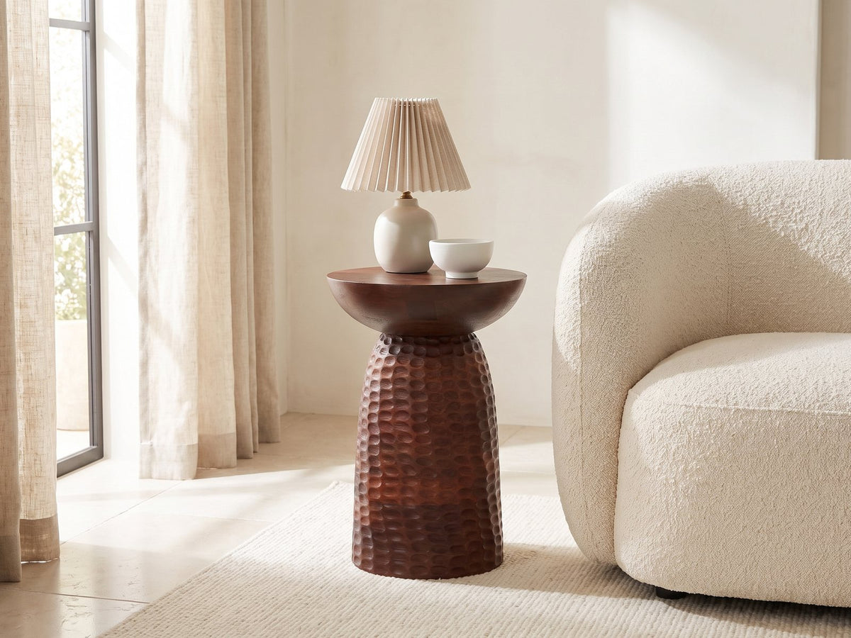 Montalbano Carved Mango Pedestal Side Table with a lamp and a ceramic bowl beside a cream boucle armchair in a bright plaster room