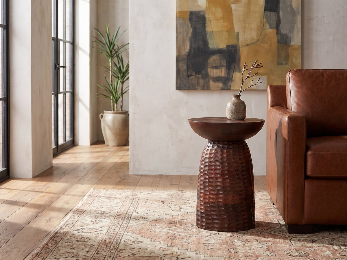 Montalbano Carved Mango Pedestal Side Table beside a leather sofa in an industrial loft