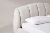 One end of the Montenerodomo headboard: the arched top edge, tall padded beige chenille channels and the thick rounded cheek, above a white pillow
