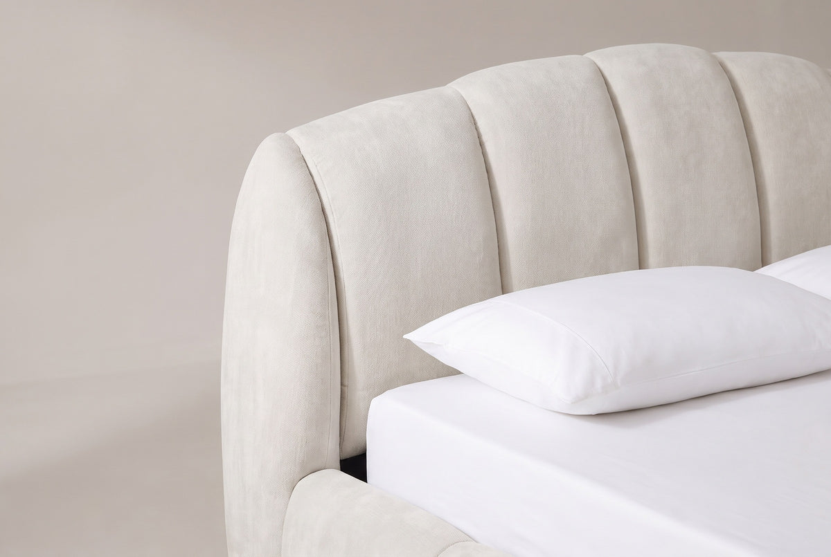 One end of the Montenerodomo headboard: the arched top edge, tall padded beige chenille channels and the thick rounded cheek, above a white pillow