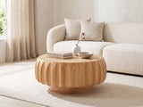 Montepulciano Fluted Ash Coffee Table seen from the side, styled with books, a vase and a stone bowl in front of a cream sofa in a bright plaster room