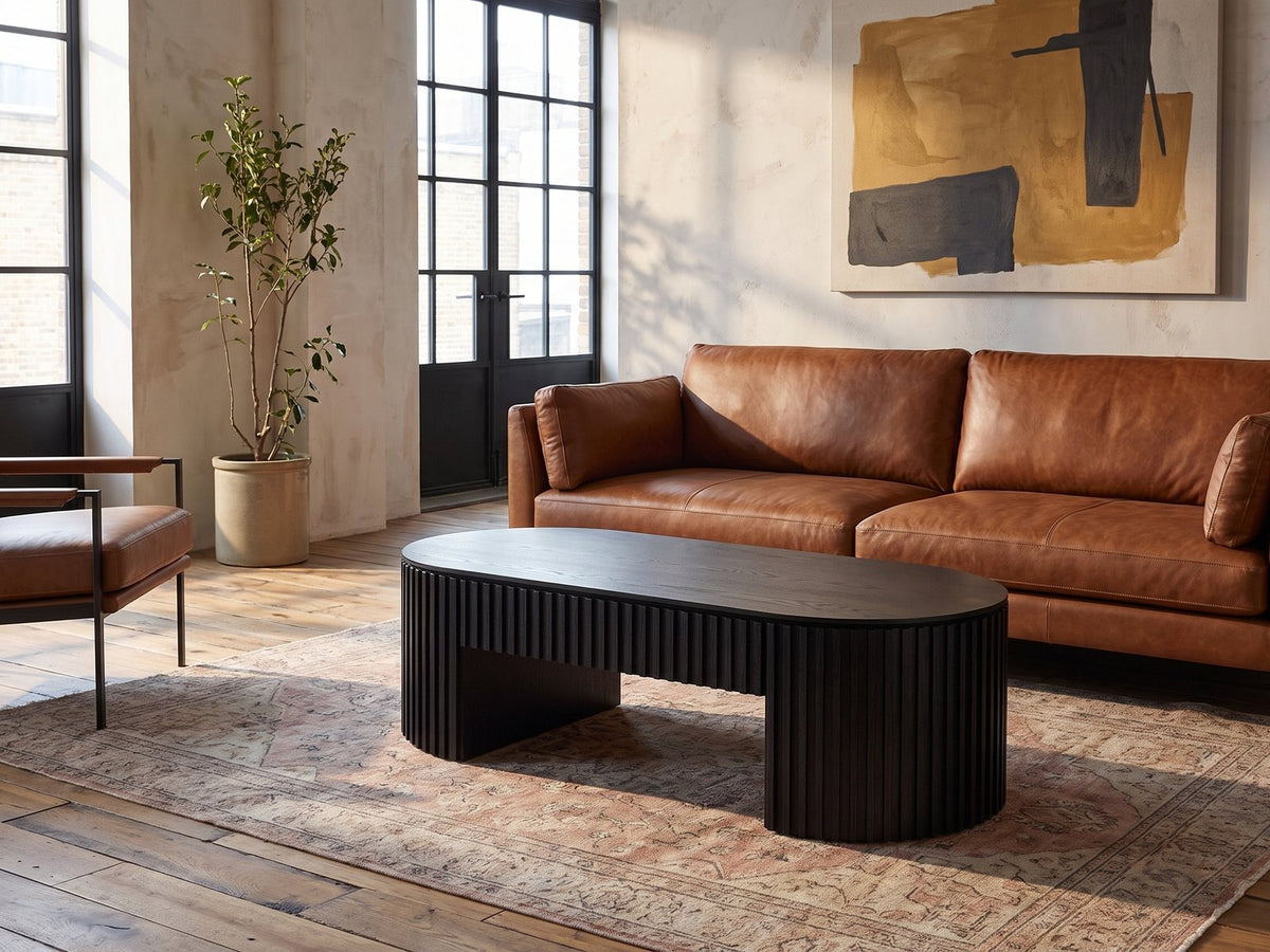 Monterosso Black Wood Veneer Fluted Oval Coffee Table on a vintage rug in front of a leather sofa in an industrial loft