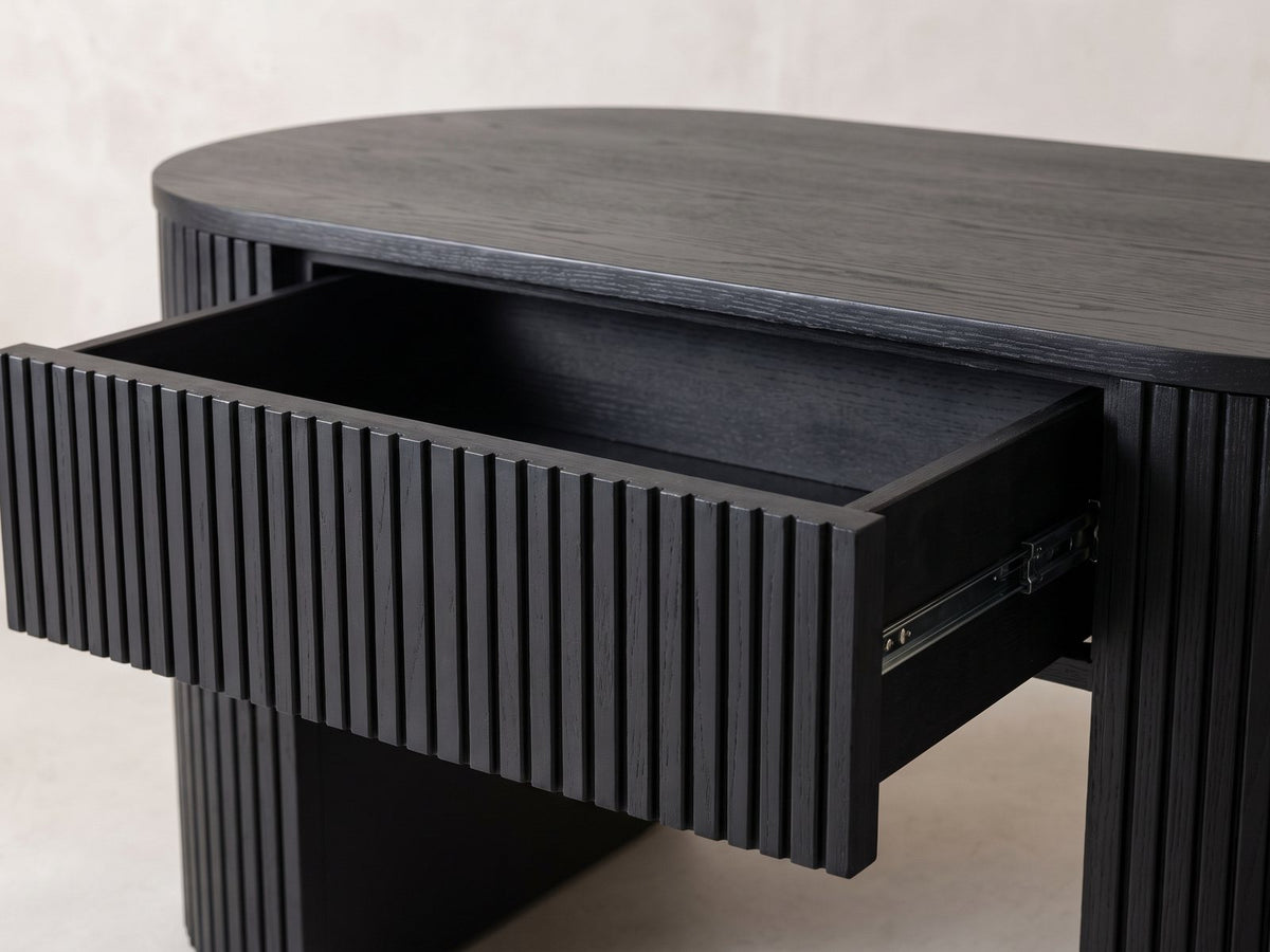 Close-up of the Monterosso Black Wood Veneer Fluted Oval Coffee Table: the slatted drawer pulled out of the fluted apron