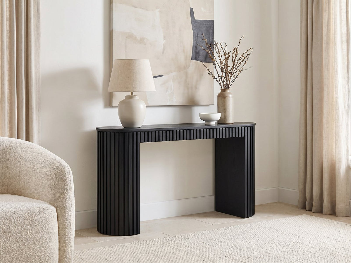 Monterosso Black Wood Veneer Fluted Oval Console Table against a plaster wall under an abstract canvas in a bright living room